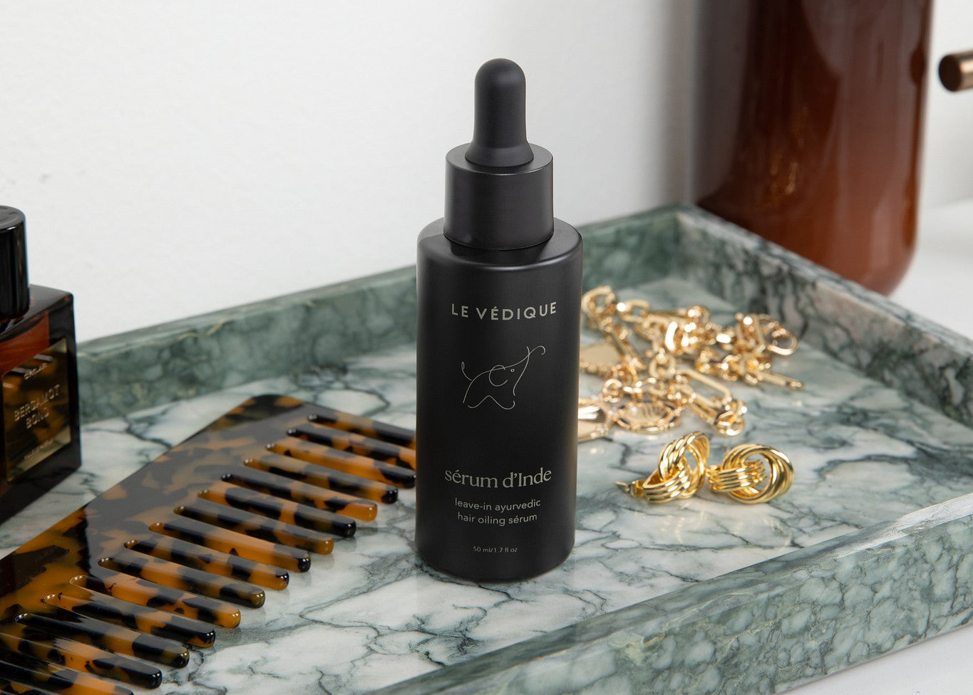 Skincare products including a dropper bottle and a brown bottle on a marble tray.